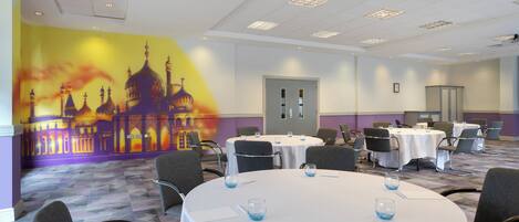 Un salón de conferencias con mesas redondas, sillas y un mural de un edificio en la pared.
