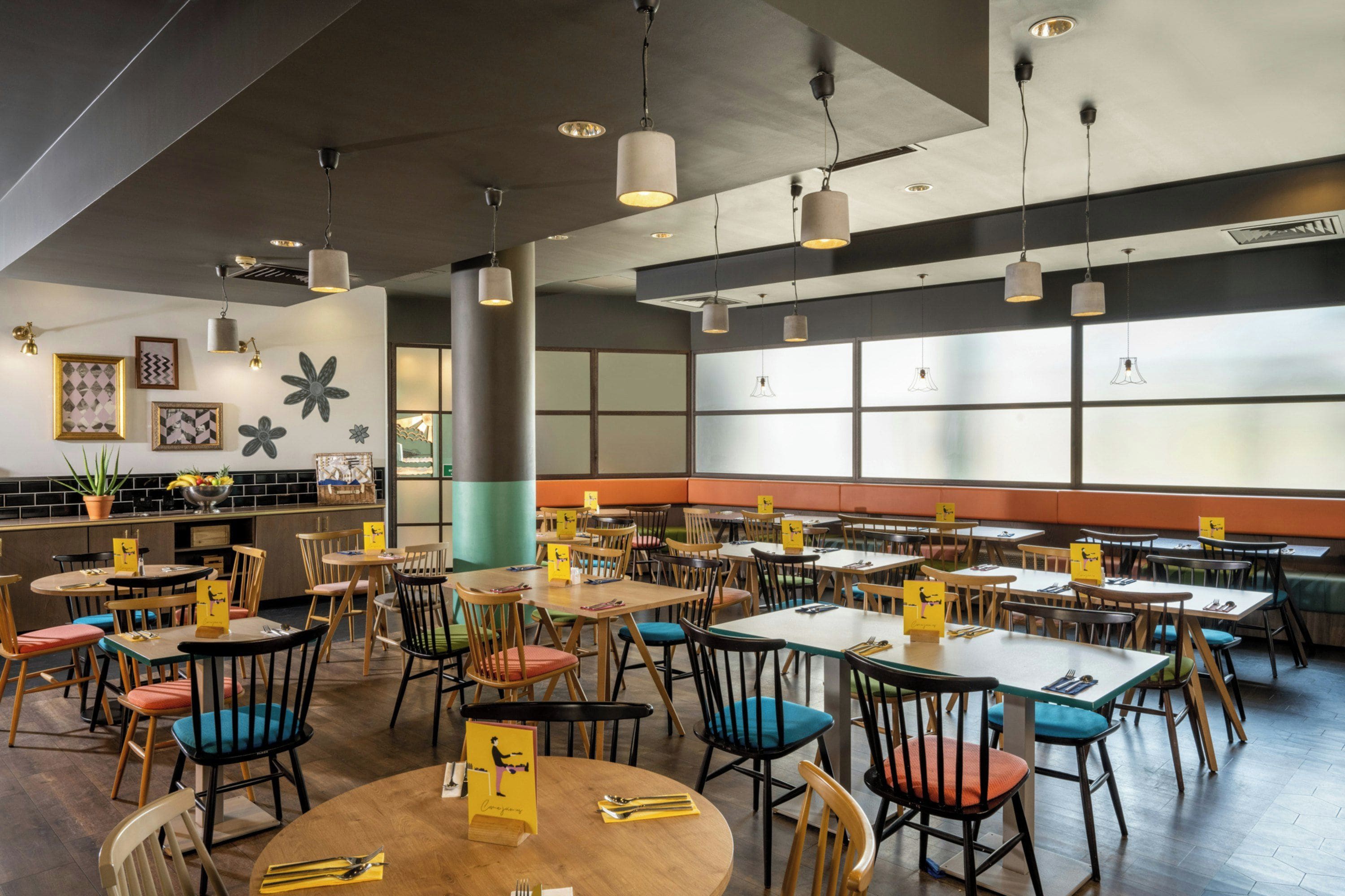 Een restaurant met ronde tafels en stoelen, een bar en een groot raam met uitzicht.