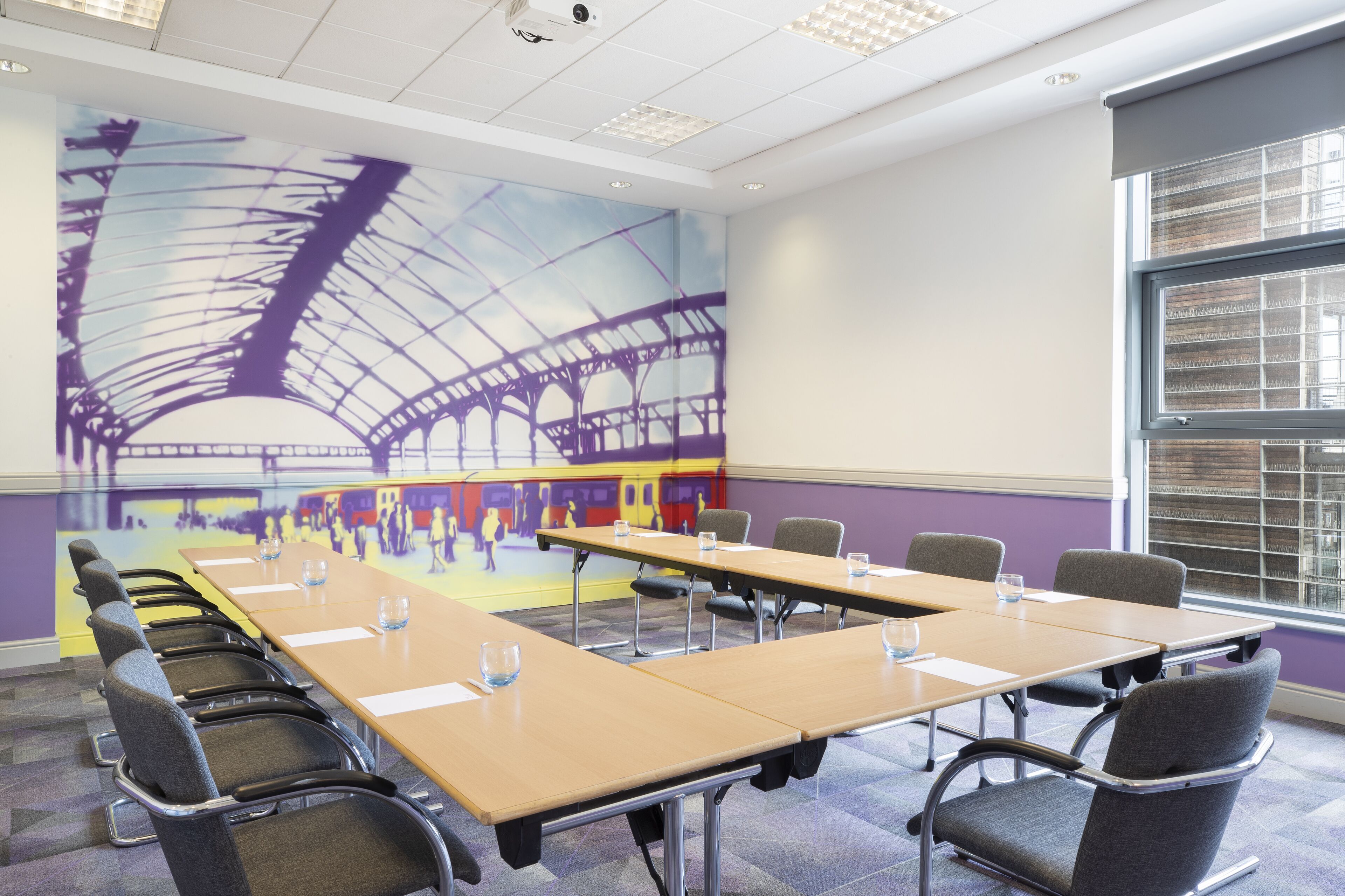 A conference room with a long table, chairs, and a mural of a bridge.