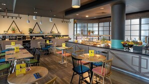 A restaurant with multiple dining tables and chairs, a buffet counter with various food items, and pendant lighting.