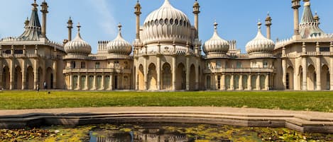 A large, ornate building with multiple domes and towers, surrounded by a well-maintained lawn and a reflective water feature.