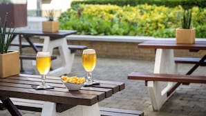 Two tables with beer glasses and a bowl of fries, set outdoors with a hedge and buildings in the background.