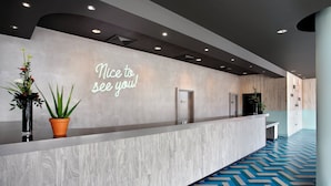 A modern reception area with a welcoming sign, a reception desk, and a patterned floor. - Leonardo Hotel Brighton (Brighton)