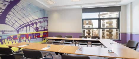 A conference room with long tables, chairs, and a large window with a view of buildings.