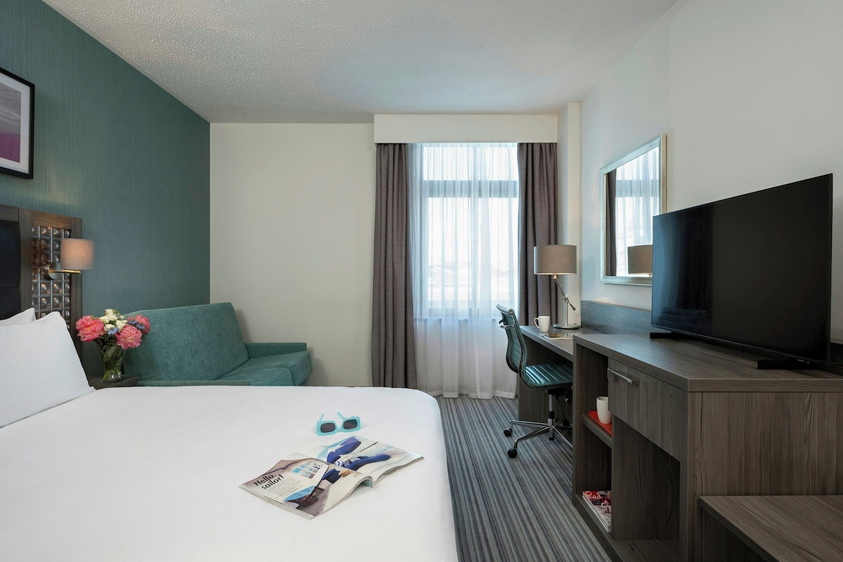 A hotel room with a bed, a desk, a television, and a window with curtains.