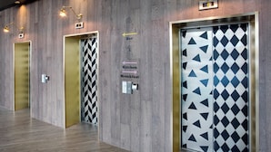 A hotel lobby with three elevators, each with a distinct door design. Directional signs indicate the bar, kitchen, and breakfast areas. - Leonardo Hotel Brighton (Brighton)