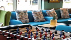 A room with a foosball table, a blue sofa with patterned cushions, and a small table with a plant.