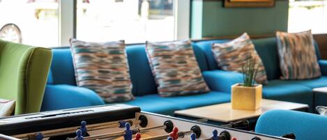 Ein Zimmer mit einem Kicker, einem blauen Sofa mit gemusterten Kissen und einem kleinen Tisch mit einer Pflanze.