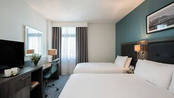 A hotel room with two beds, a desk with a TV, and a window with curtains.