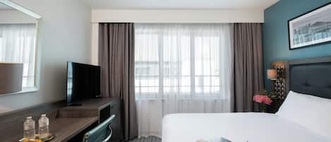 A hotel room with a bed, a desk, a television, a chair, and a window with curtains.