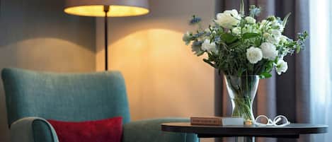 Une chambre d’hôtel avec un fauteuil turquoise, une petite table d’appoint sur laquelle se trouve un vase de fleurs, une lampe et un livre intitulé « 10 000 ans d’art ».