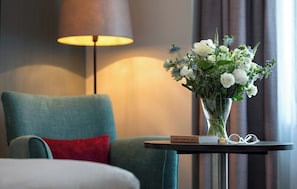 A hotel room with a teal armchair, a small side table with a vase of flowers, a lamp, and a book titled '10,000 Years of Art'. - Leonardo Hotel Brighton (Brighton)