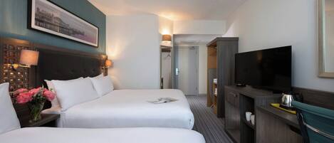 A hotel room with two beds, a television, a desk with a lamp, and a framed picture on the wall.