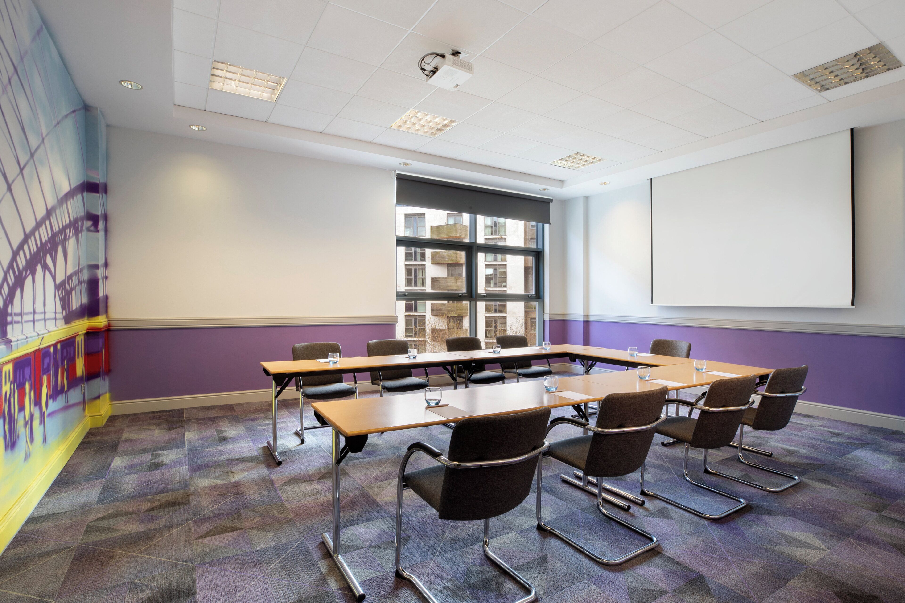 A conference room with a long table, chairs, a projector screen, and large windows.
