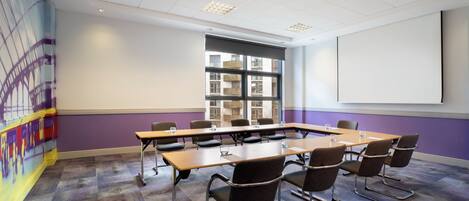 A conference room with a long table, chairs, a projector screen, and large windows.