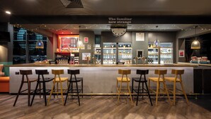 A bar area with a counter, stools, and shelves with bottles. - Leonardo Hotel Brighton (Brighton)