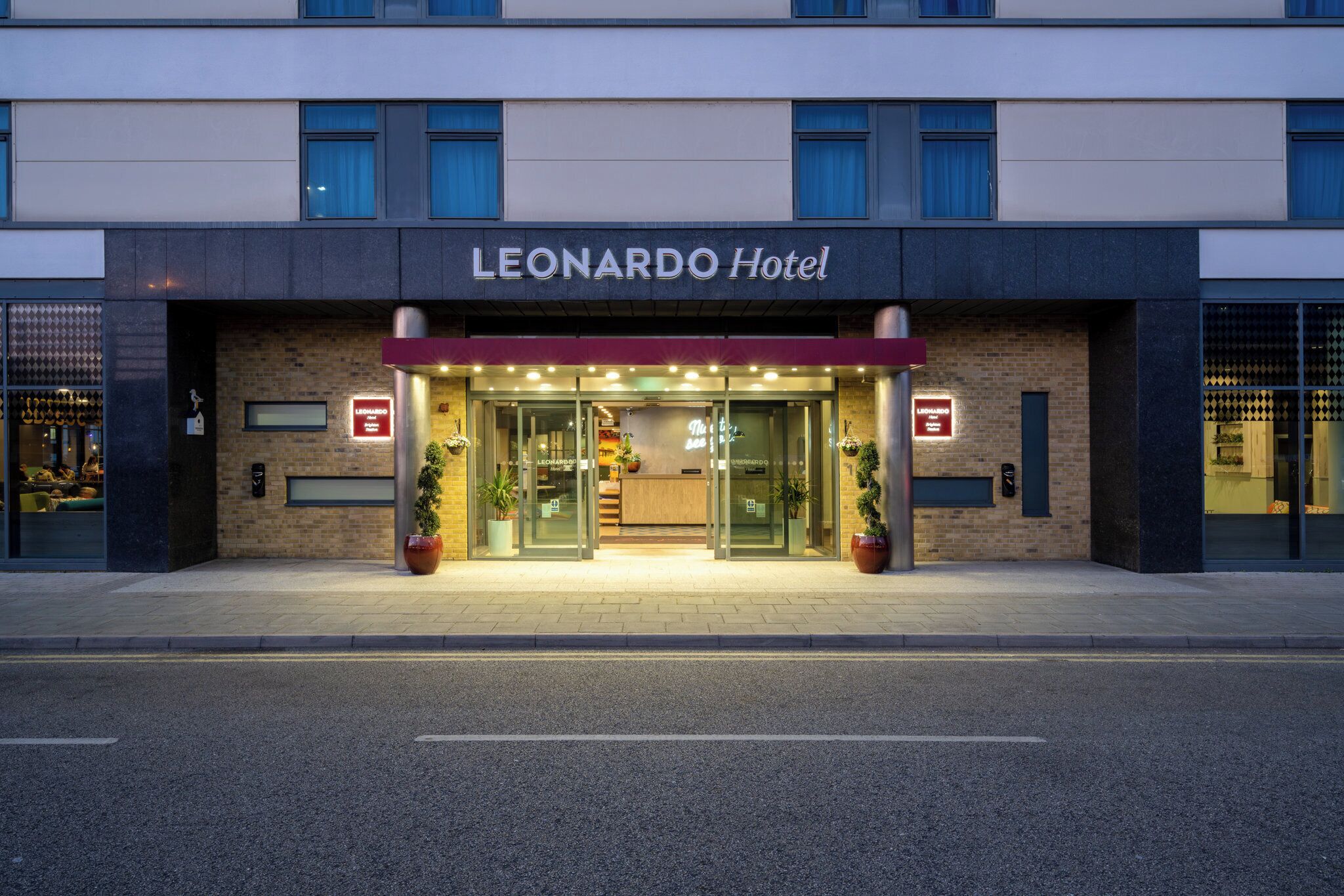 L’extérieur de l’hôtel Leonardo présente une façade moderne, une grande entrée vitrée et des plantes en pot disposées à l’entrée.