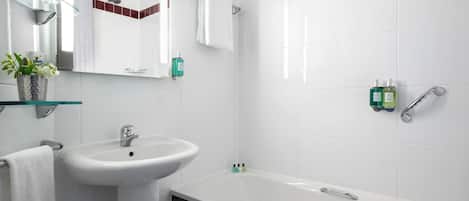 A modern bathroom with a white sink, a glass shelf with toiletries, a large mirror, and a bathtub.