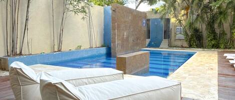 Un espace piscine avec une piscine bleue, une terrasse en bois et des meubles d’extérieur de couleur beige.