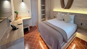 Una habitación de hotel con cama, tocador con espejo, armario y una planta pequeña.
