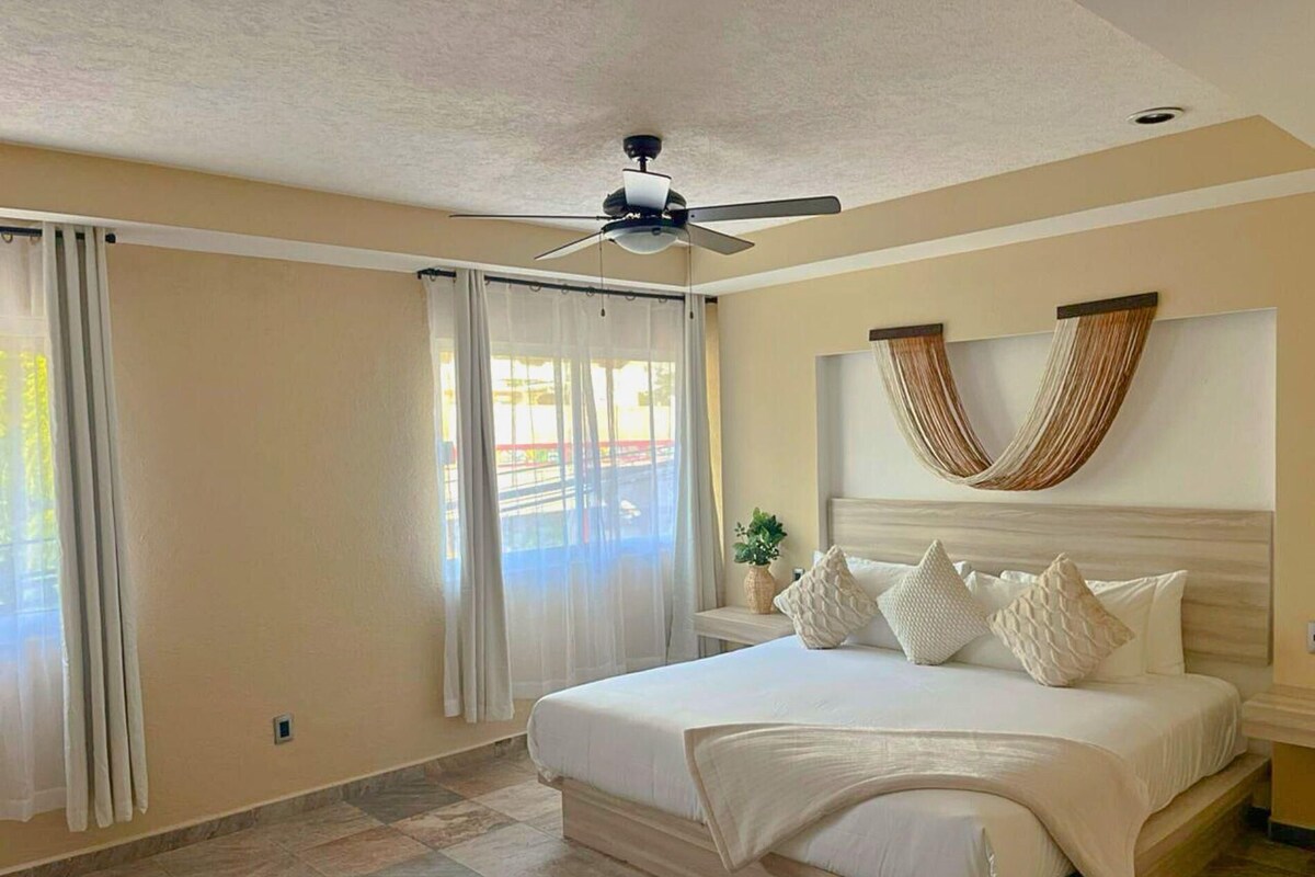 A bedroom with a bed, curtains, a ceiling fan, and a view through the window.