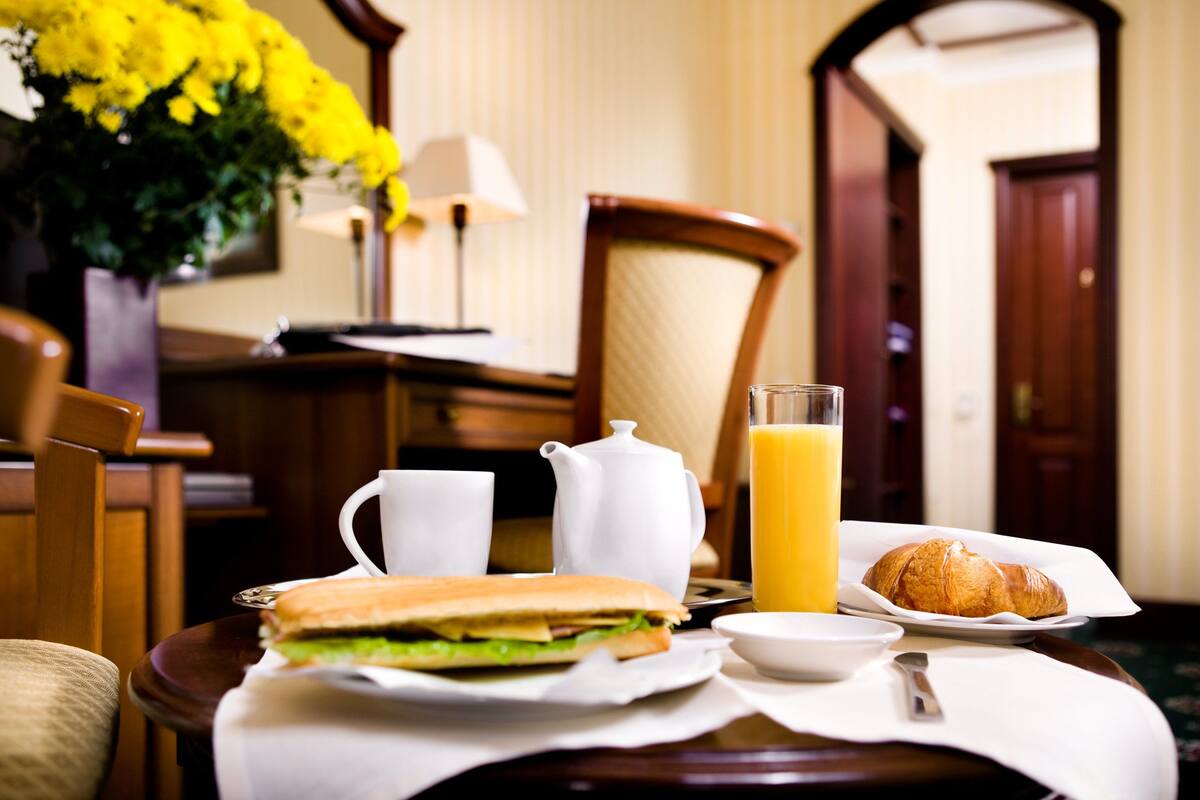 Et morgenmåltid med en sandwich, croissant, juice og en tepotte på et bord.