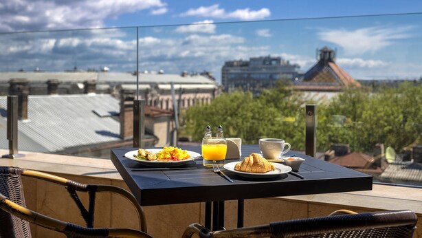 A table with breakfast items including eggs, toast, and orange juice, overlooking a cityscape with traditional architecture. - Ayvazovsky (Odesa)