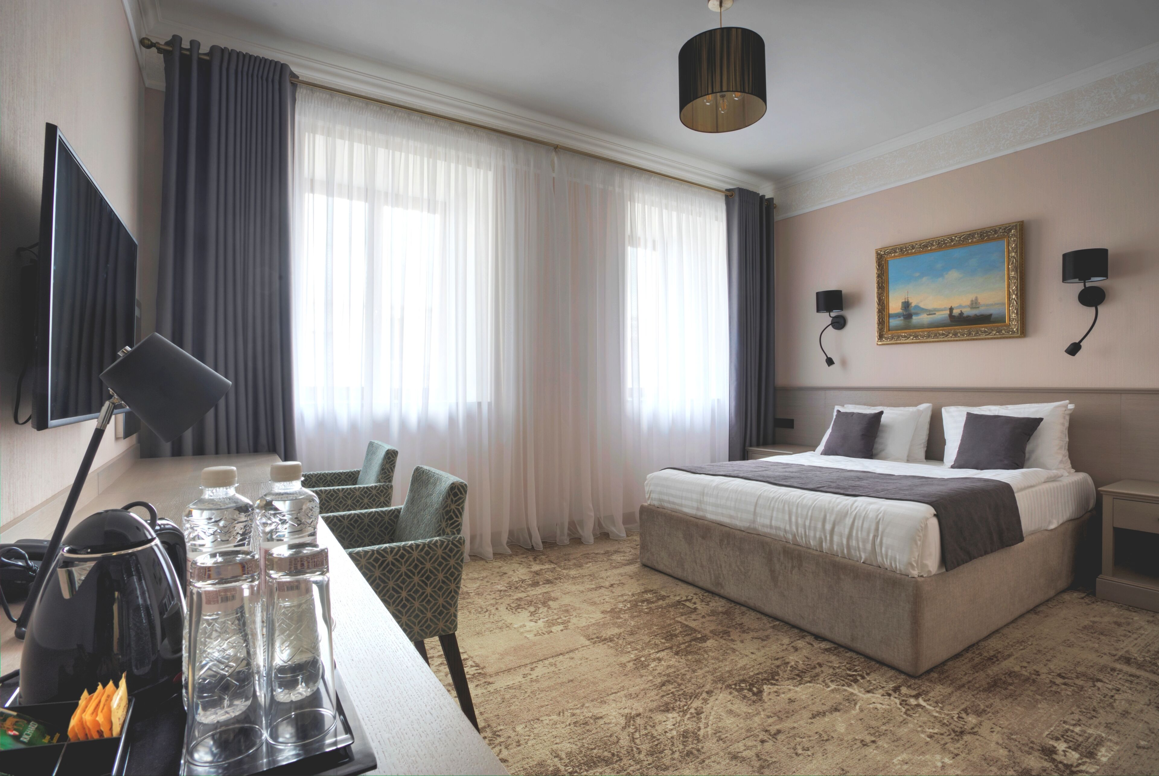 A hotel room with a bed, a desk with a lamp, a chair, a television, and a painting on the wall.