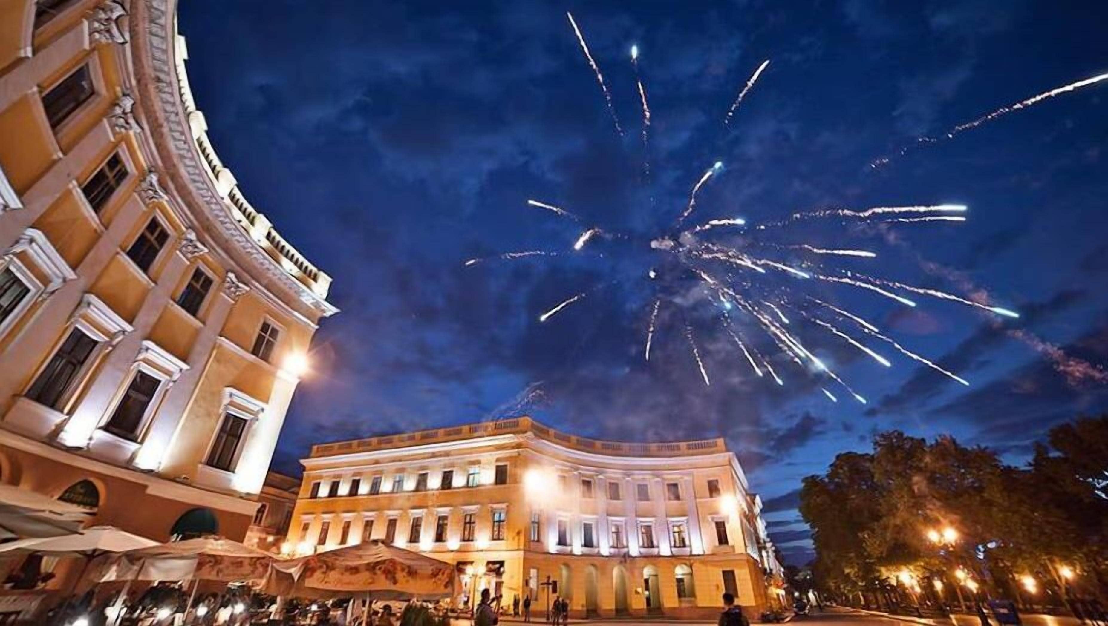 A historic building with classical architecture, a public square, and a night sky with fireworks.