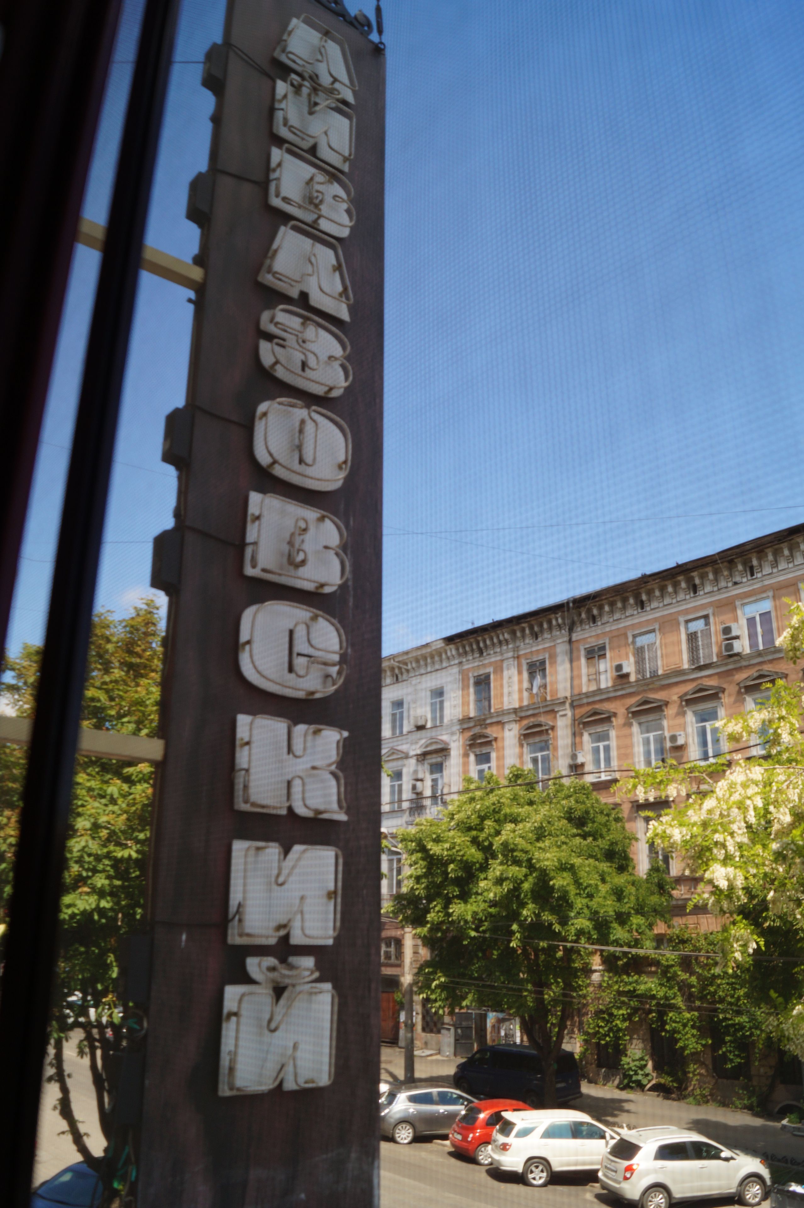 Fachada de edificio con una serie de ventanas numeradas y vista de la calle con coches aparcados y árboles.