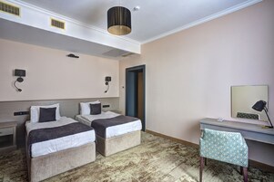 Habitación de hotel con dos camas, un escritorio, una silla, una lámpara de escritorio, un espejo y una puerta.
