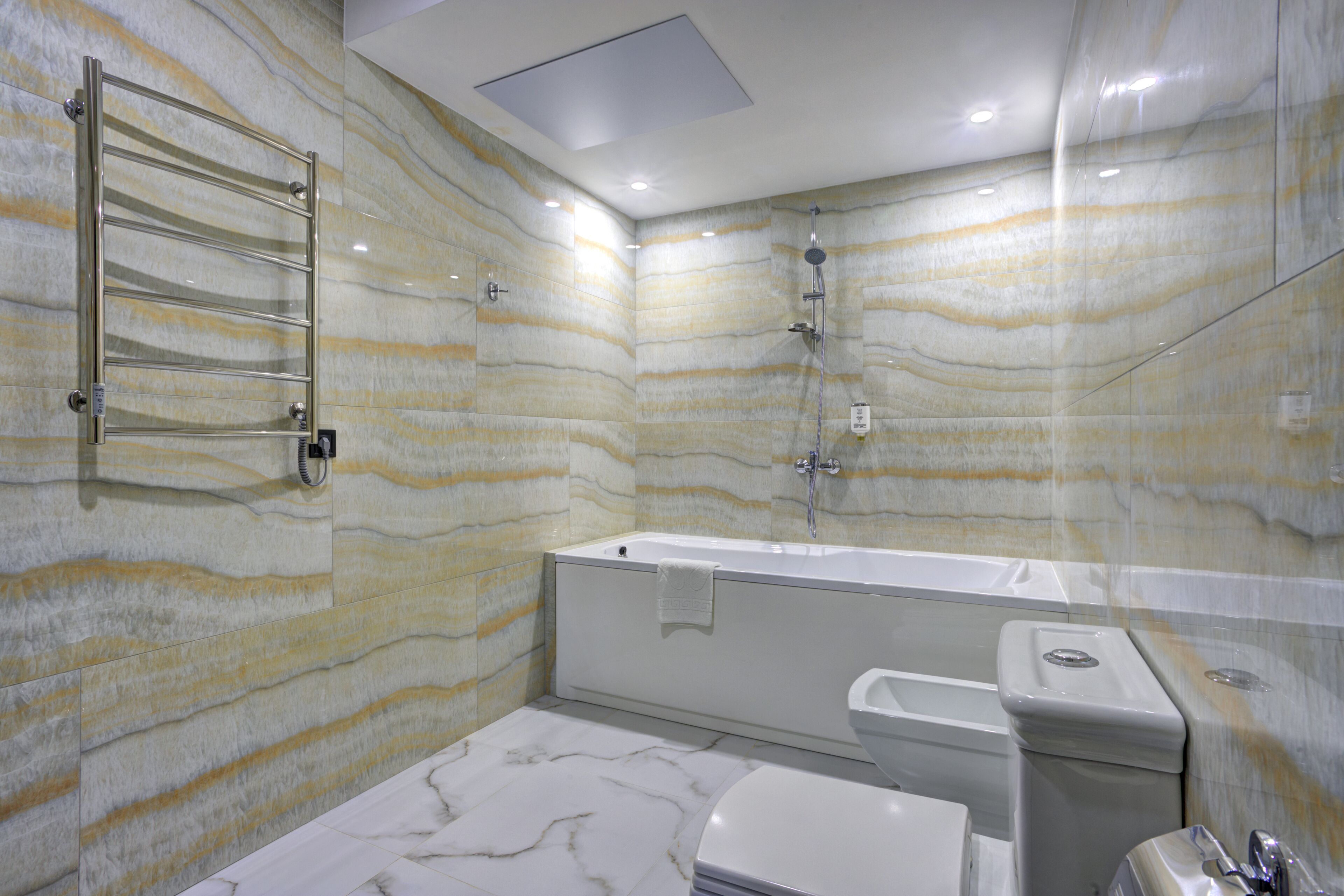 Um banheiro com parede estampada em mármore, uma banheira, vaso sanitário e chuveiro.