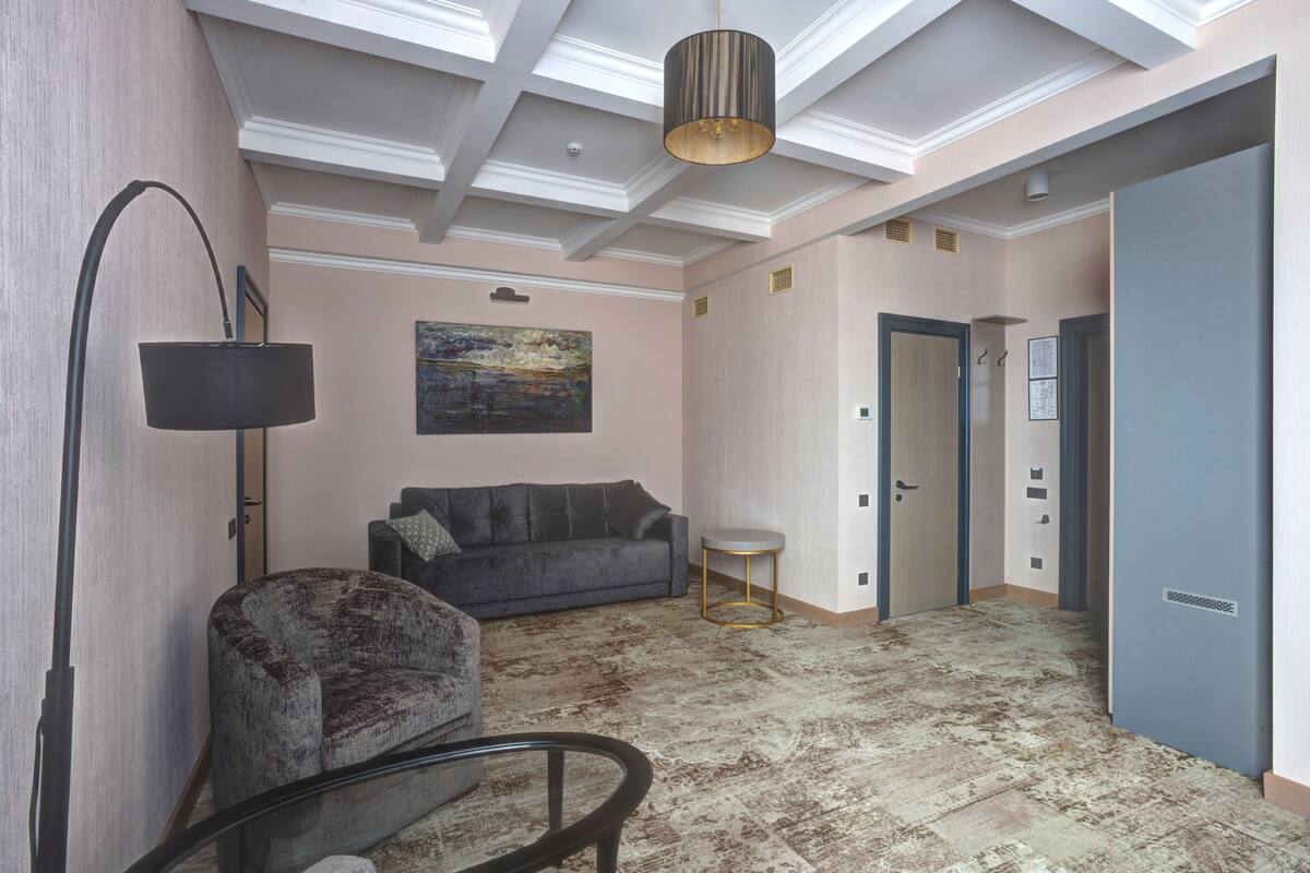 En rummelig opholdsstue med en grå sofa, en stilet lænestol, et glasbord og en moderne pendellampe.