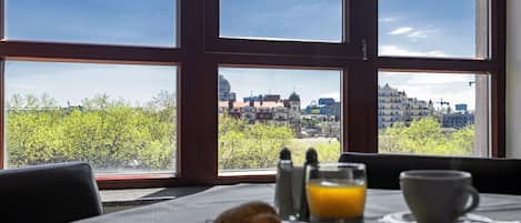 A breakfast setup with croissant, orange juice, and coffee on a table with a city view through large windows.