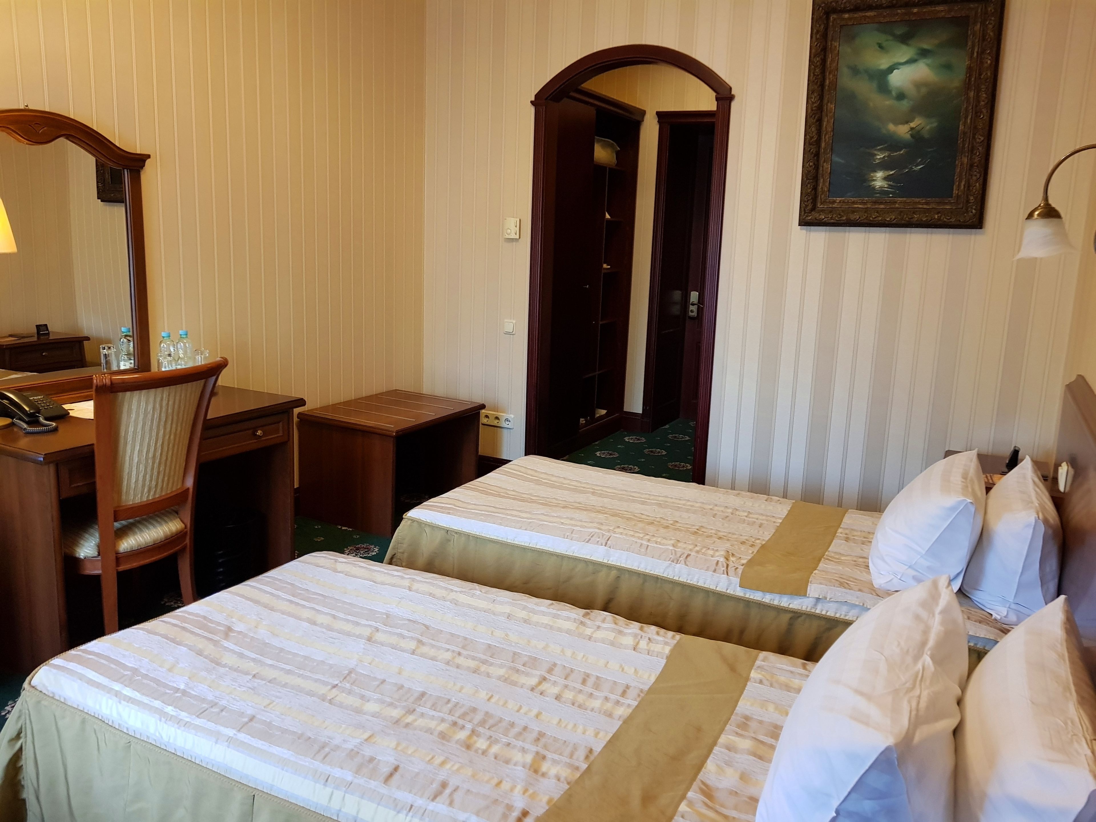 Habitación de hotel con dos camas, un escritorio, una silla, una lámpara y un cuadro en la pared.