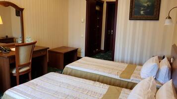 Habitación de hotel con dos camas, un escritorio, una silla, una lámpara y un cuadro en la pared.