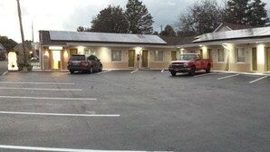 A motel with a parking lot, several vehicles parked, and a sign for a nearby establishment. - Lodge Inn (Wrightstown)