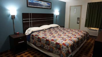 A hotel room with a large bed, a nightstand, a wall-mounted clock, a framed picture, and an air conditioning unit.