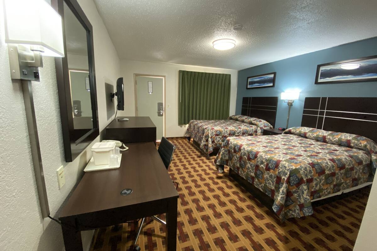 A hotel room with a desk, two beds, a mirror, a telephone, and a headboard with a light.