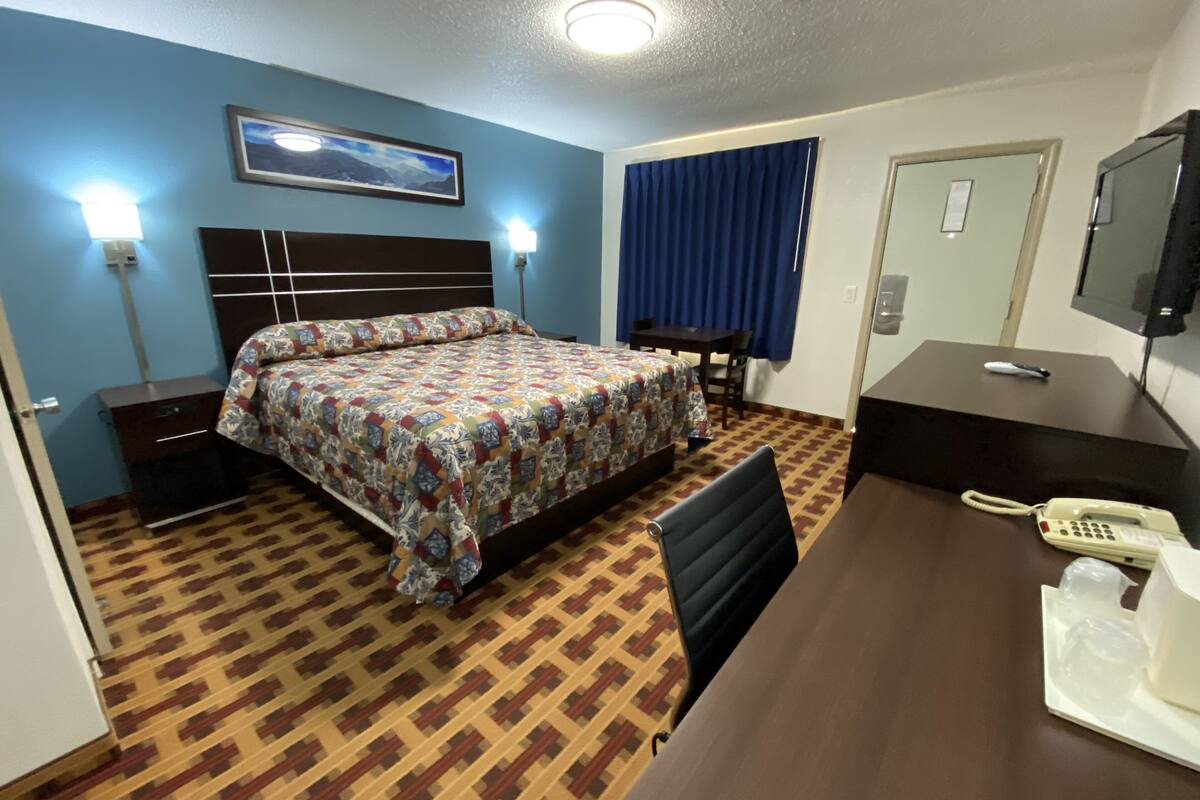 A hotel room with a bed, bedside table, desk, chair, and a telephone.