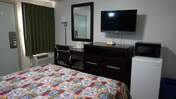 Habitación de hotel con cama, escritorio, televisor, microondas y refrigerador pequeño.