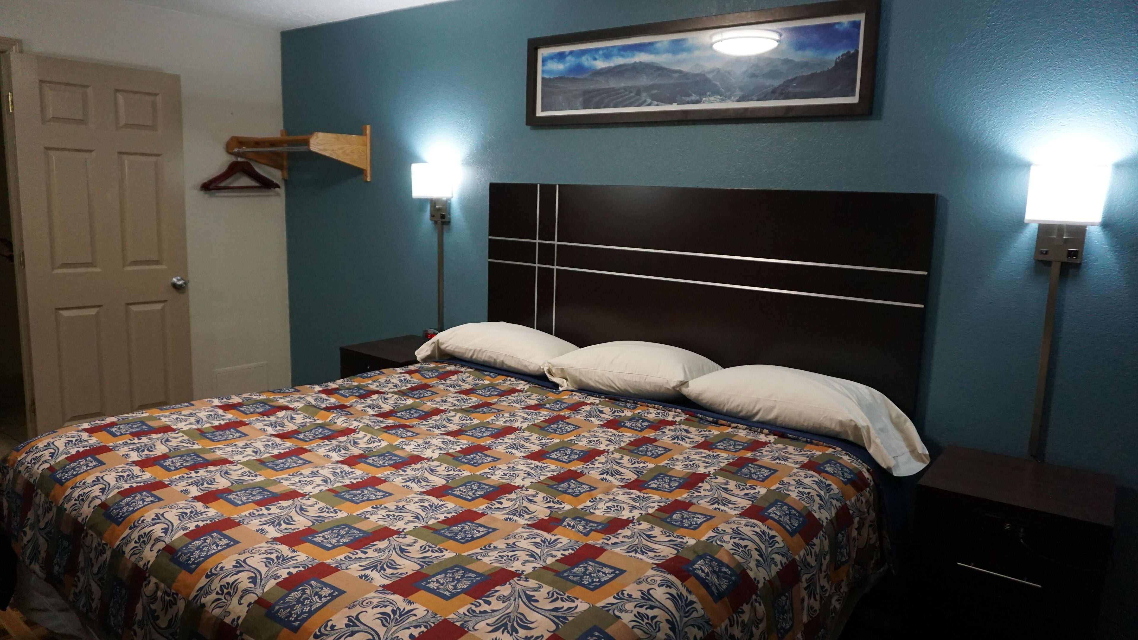 A bedroom with a bed, a nightstand, a wall-mounted lamp, and a door.