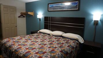 A bedroom with a bed, a nightstand, a wall-mounted lamp, and a door.