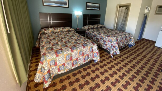A hotel room with two beds, a headboard with a light fixture, a wall-mounted picture, and a patterned carpet. - Lodge Inn (Wrightstown)