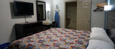 Una habitación de hotel con cama, cómoda, televisión, escritorio y espejo.