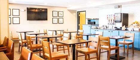 A restaurant with multiple tables and chairs, a kitchen area, and framed artwork on the walls.
