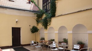 A courtyard with a tiled floor, metal chairs, a table, potted plants, and a door. - Hotel King George (Prague)
