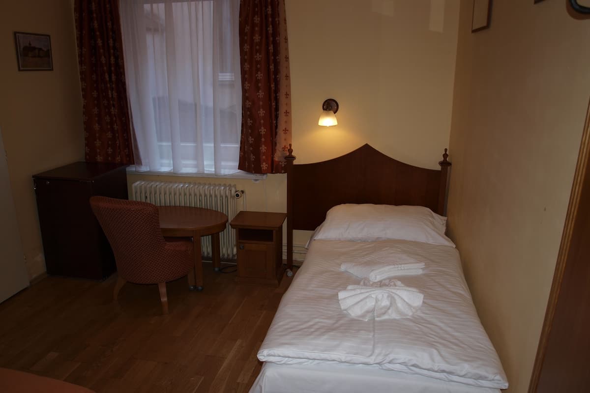 Una camera d'albergo con un letto, una scrivania, una sedia, un termosifone e una lampada a parete.