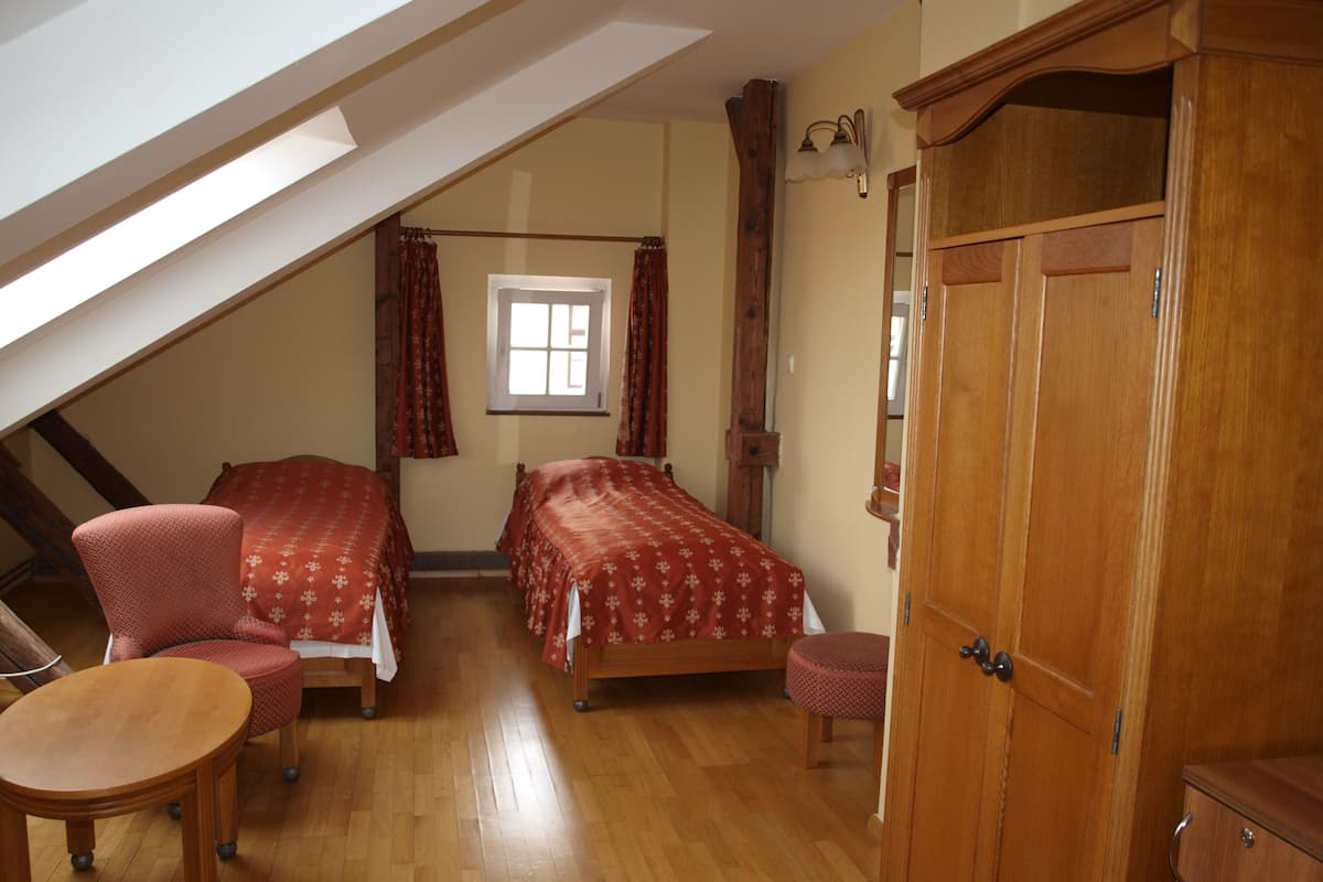 Un dormitorio con dos camas, un armario de madera, una mesita, una silla y una ventana con cortinas.