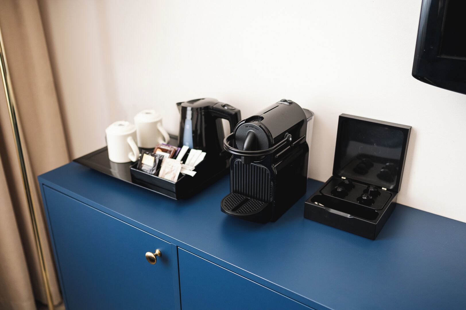 Une machine à café, un service à thé et une boîte posés sur un meuble bleu.